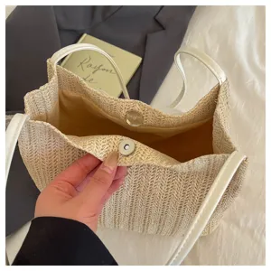 Detail shot of a woven straw tote bag with white shoulder straps and magnetic closure.