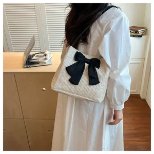 Detailed view of the chic straw shoulder bag featuring a large black bow, shown in a cozy room setting.
