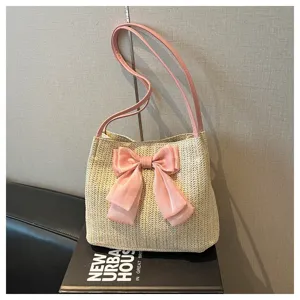 Close-up detail of the straw woven shoulder bag featuring a large pink bow and straps.