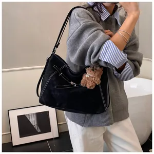 Close-up of black suede shoulder bag with contrast white stitching and cute teddy bear charm.