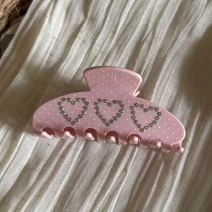 Primo piano della molletta per capelli rosa con cuori in strass, dettaglio pois carino.