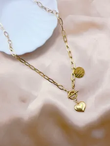 Dettaglio collana con catena maglia ovale dorata, ciondolo a cuore e medaglietta incisa.