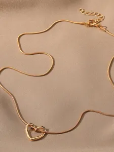 Primo piano di una collana con ciondolo a cuore vuoto dorato su tessuto satinato.