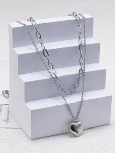 Dettaglio di collana a doppia catena in acciaio al titanio argentato con ciondolo a cuore.
