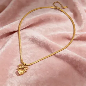 Gros plan détaillé du collier élégant doré avec pendentif nœud et cœur sur velours rose.