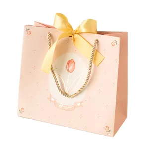 Bolsa de regalo de papel rosa con lazo amarillo y estampado de tulipanes para fiestas.