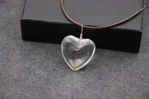 Close-up van een handgemaakte transparante hartvormige hanger met echte paardenbloem