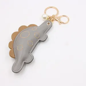 Close-up detail of the cute dinosaur leather keychain with gold hardware and pearl pendant.