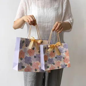 Elegantes bolsas de regalo de papel floral con lazos dorados para cumpleaños y días festivos.