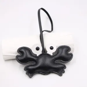 Detailed closeup of a cute black leather crab bag charm with black strap and white eyes.