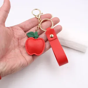 Red apple leather keychain detail view, featuring gold hardware and matching strap pendant.