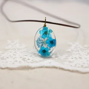 Primer plano detallado de un collar con colgante de resina ovalada con flores secas azules.
