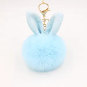 Close-up of light blue fluffy rabbit ear pom pom keychain with gold metal hardware detail.