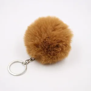 Brown faux fur pom pom keychain detail shot, fluffy ball bag charm and car pendant close up.