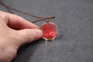 Close-up detail of a handmade dried flower resin pendant necklace featuring red preserved flora.