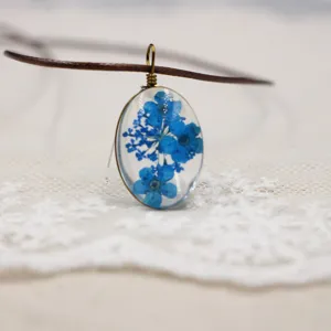 Vista detallada de un collar con colgante ovalado de resina y flores secas azules.