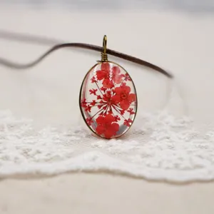 Primer plano detalle colgante ovalado de resina con flores rojas prensadas, delicada joya artesanal.