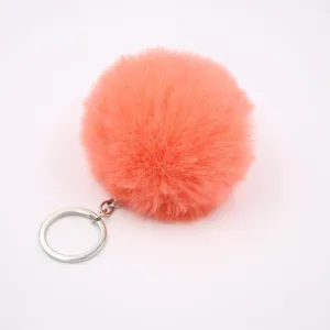 Close-up of fluffy orange pom pom keychain with silver metal ring, soft artificial fur texture.