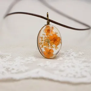 Detalle del hermoso collar con colgante de flor seca de resina ovalada con cordón marrón.