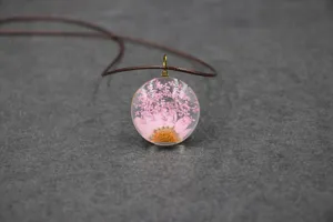 Close-up detail of handmade pressed flower resin pendant necklace with pink floral botanicals inside.