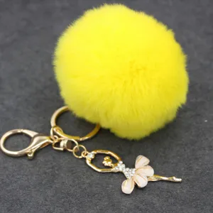 Llavero de pompón de felpa amarilla con colgante de bailarina de diamantes y herrajes dorados.