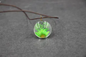Glass resin dried flower pendant detail shot, green floral botanical necklace close up view.
