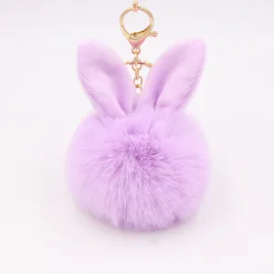 Close-up of fluffy purple bunny ears pompom keychain charm with gold metal clasp detail.