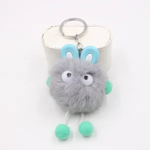 Close-up detail of the cute grey fluffy plush keychain with blue ears and dangling green feet.