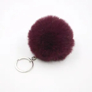 Faux fur pom pom keychain detailed shot, wine red fluffy ball charm for bags and car keys.