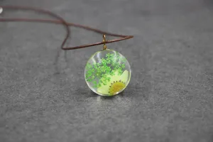 Close-up of a clear resin pendant necklace featuring real dried green flowers and plants inside.