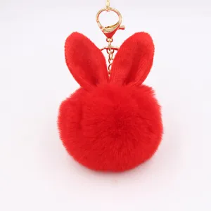 Close up of red plush rabbit ear pompom keychain with gold hardware detail bag pendant.