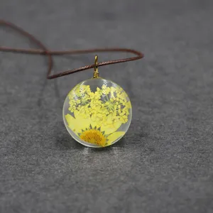 Close-up detail of the clear resin round pendant featuring delicate yellow dried flowers.