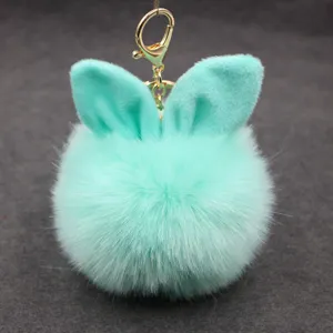 Close-up detail of fluffy mint green rabbit ear pom pom keychain with gold clasp accessory.