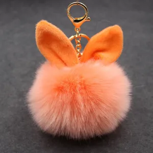 Close-up detail of the fluffy orange pom-pom keychain with plush rabbit ears and gold clasp design.