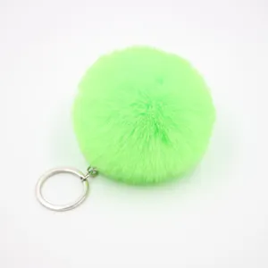 Green faux fur pom pom keychain detail, soft fluffy plush bag charm and car pendant accessory.