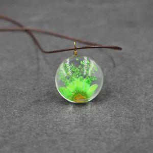 Glass sphere pendant detail featuring green pressed dried flowers and brown leather cord necklace.