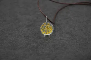 Detailed closeup of handmade dried yellow flower glass globe pendant necklace on brown cord.