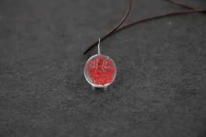 Close-up view of handmade transparent glass ball pendant necklace with vibrant red dried flowers.