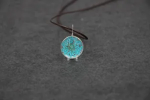 Detailed close-up of a handmade dried flower glass ball pendant necklace on brown cord.