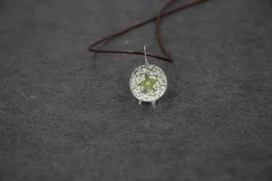 Handmade dried flower glass ball necklace close up, clear resin pendant with white lace flowers.