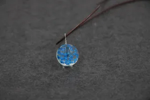 Close-up detail of a handmade glass ball pendant necklace featuring delicate blue dried flowers.