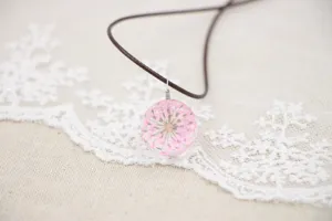 Handcrafted dried flower resin glass pendant necklace with pink lace flower detail and brown cord.