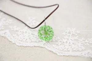 Handmade glass sphere pendant close up featuring delicate green dried flowers inside.