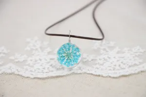 Close-up of handmade dried flower glass ball necklace detail, blue eternal flower pendant.