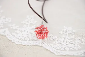 Handmade dried flower glass ball necklace detail close-up, red floral pendant on cord.