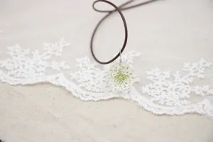 Handmade dried flower necklace detail view with glass ball pendant and white floral.
