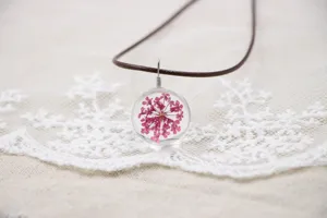 Handcrafted dried flower glass ball necklace detail featuring pink floral pendant and brown cord.