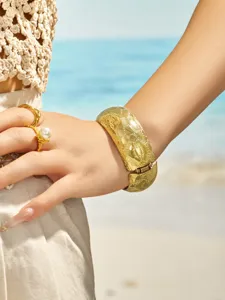 Close-up detail of wide gold stainless steel cuff bracelet with frosted texture on model wrist.