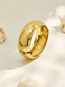 Detailed close-up of a wide gold plated stainless steel frosted textured hinged bangle bracelet.