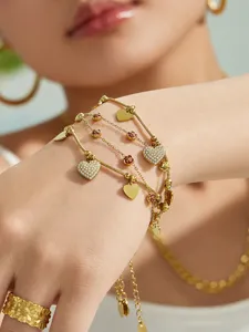 Vista detallada de la pulsera multicapa de acero dorado con circonita de corazón en muñeca